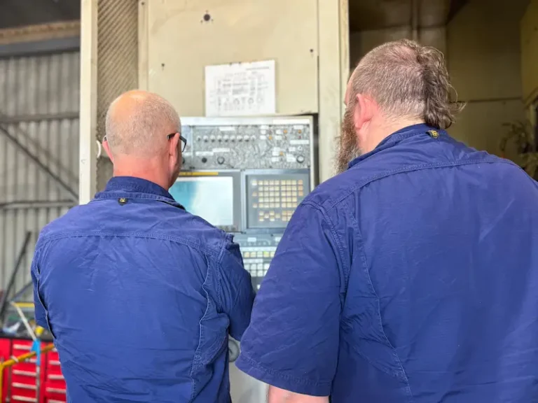 Two ABCO Precision Machining employees working side-by-side programming a CNC milling machine in the Brisbane headquarters